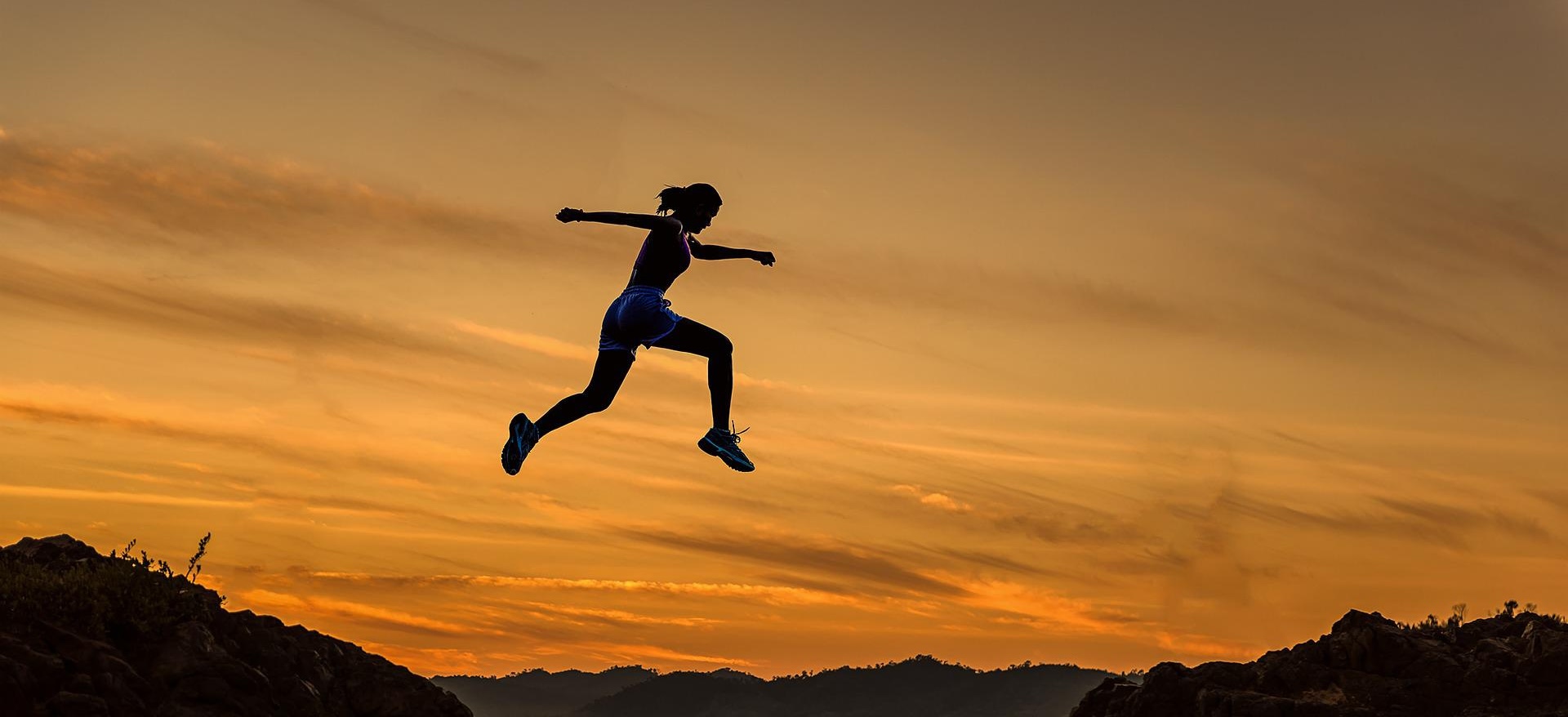 Frau springt vor einem Abendhimmel